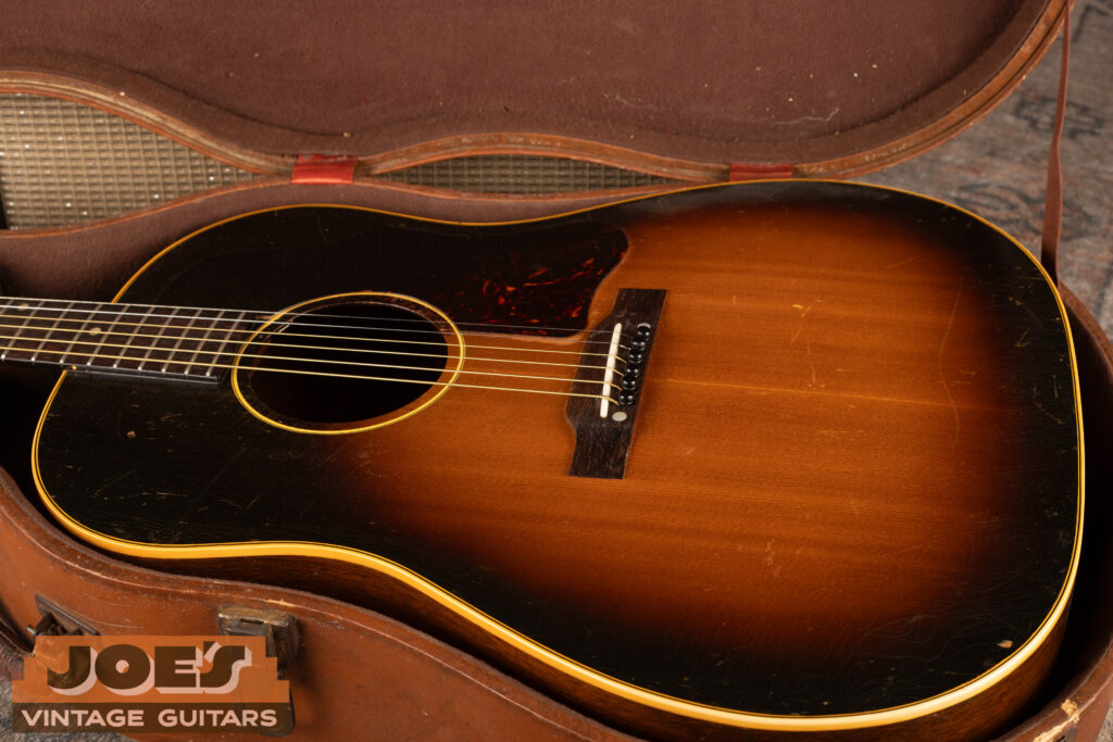 A vintage 1950s Gibson J-45 "Workhorse" acoustic guitar with a sunburst finish and original teardrop pickguard resting in its case at Joe's Vintage Guitars