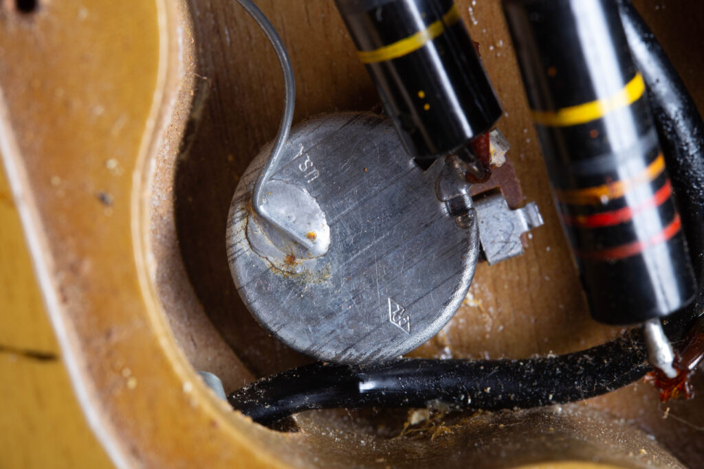 Close-up of an original 1958 Centralab (CRL) potentiometer inside a Gibson Les Paul Special control cavity. The metal casing clearly shows the stamped "USA" text and the small characteristic diamond CRL logo. The component is wired with original period-correct solder and a Bumblebee capacitor, set against the mahogany wood grain of the internal routing.